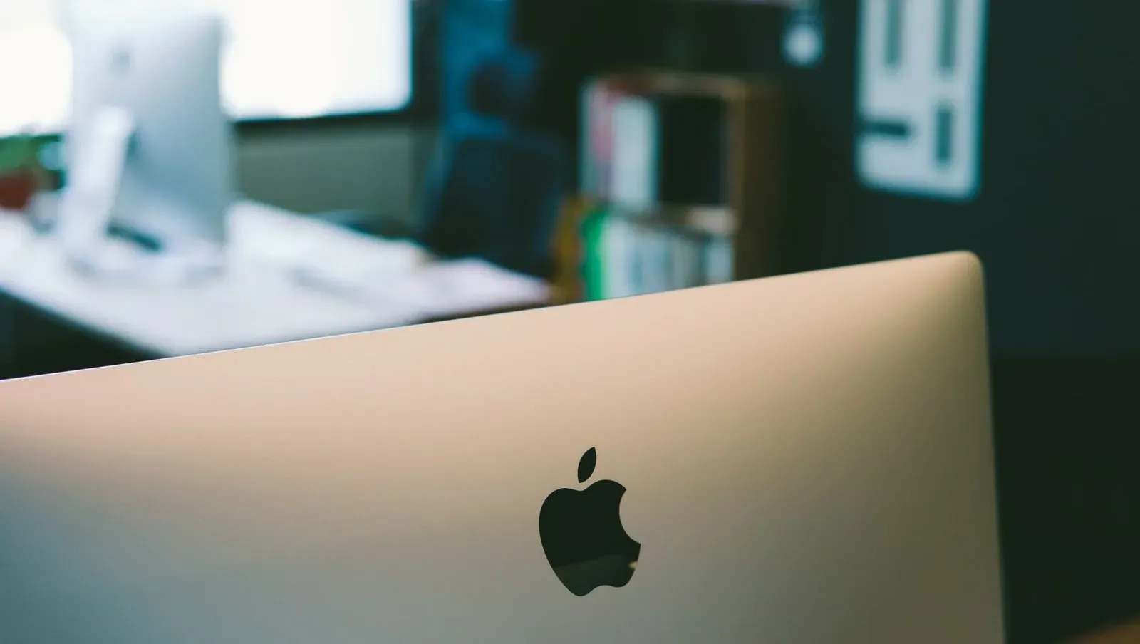 Rear view of an Apple desktop computer with the logo in focus in a blurred office setting.